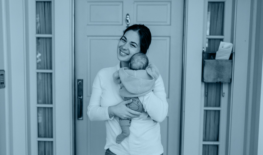 young woman holding a baby, standing in front of a front door